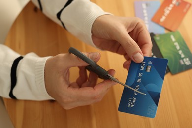 Photo of Woman cutting credit card at wooden table indoors, closeup