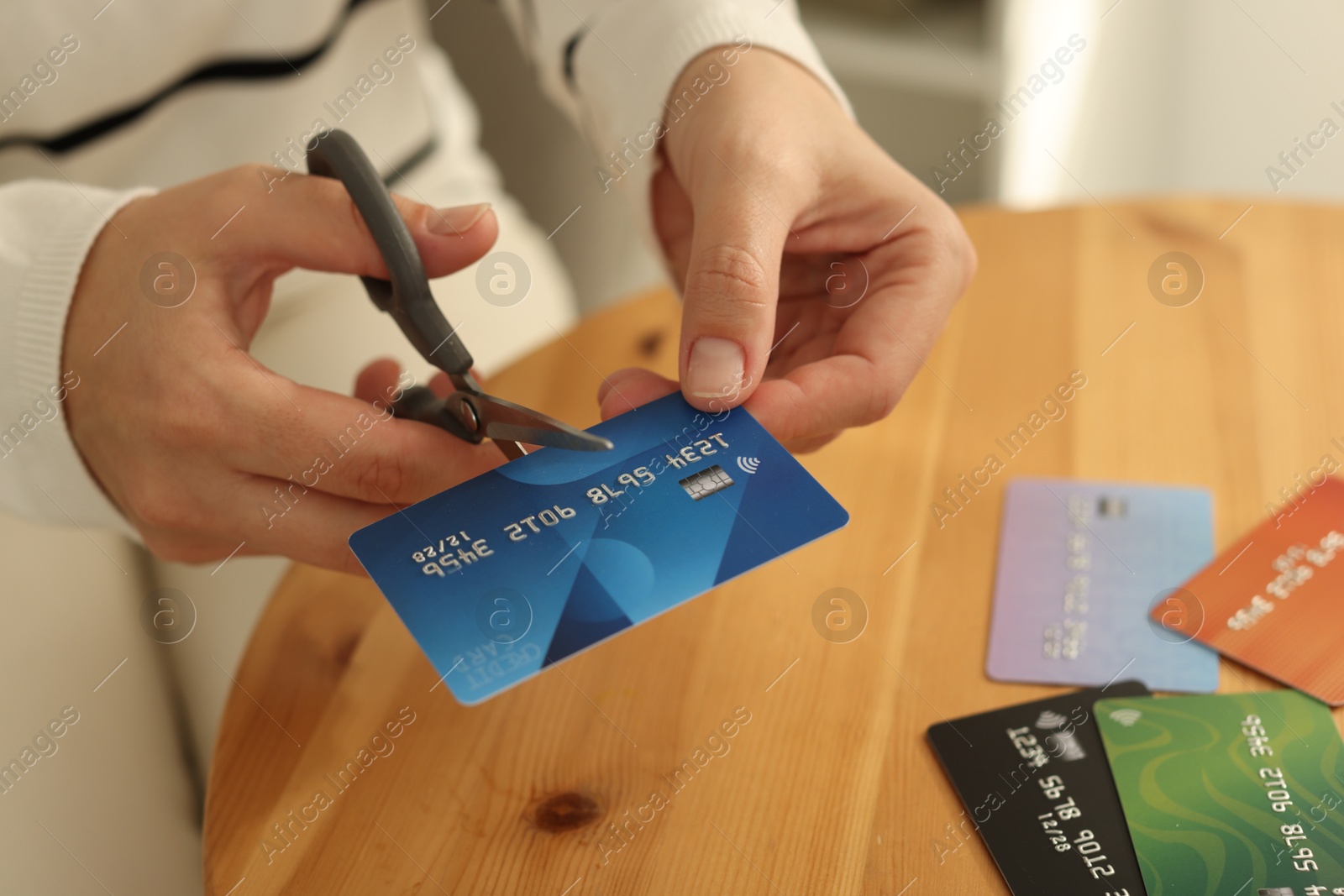 Photo of Woman cutting credit card at wooden table indoors, closeup