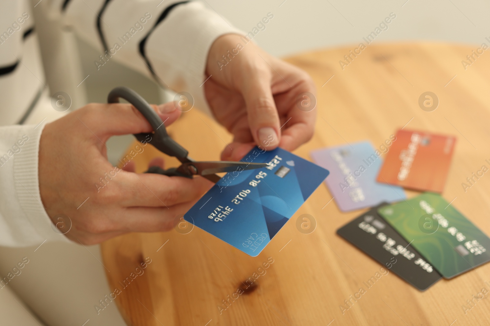 Photo of Woman cutting credit card at wooden table indoors, closeup