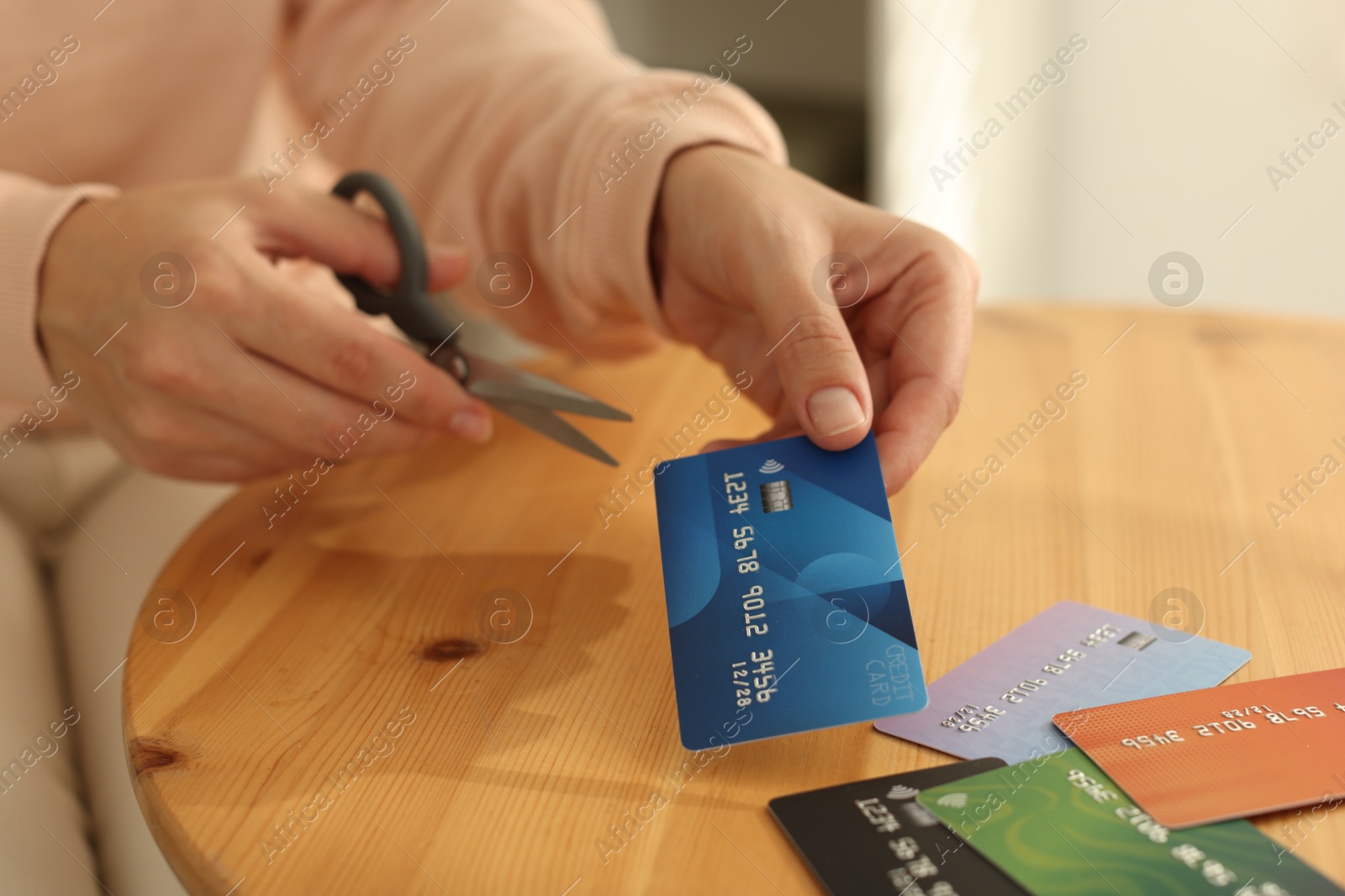 Photo of Woman cutting credit card at wooden table indoors, closeup