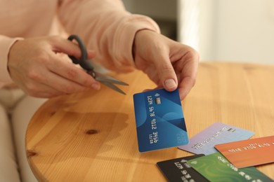 Photo of Woman cutting credit card at wooden table indoors, closeup