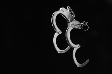 Photo of Metal chain handcuffs on black background, closeup. Space for text