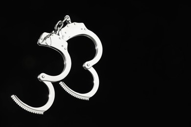 Photo of Metal chain handcuffs on black background, closeup. Space for text