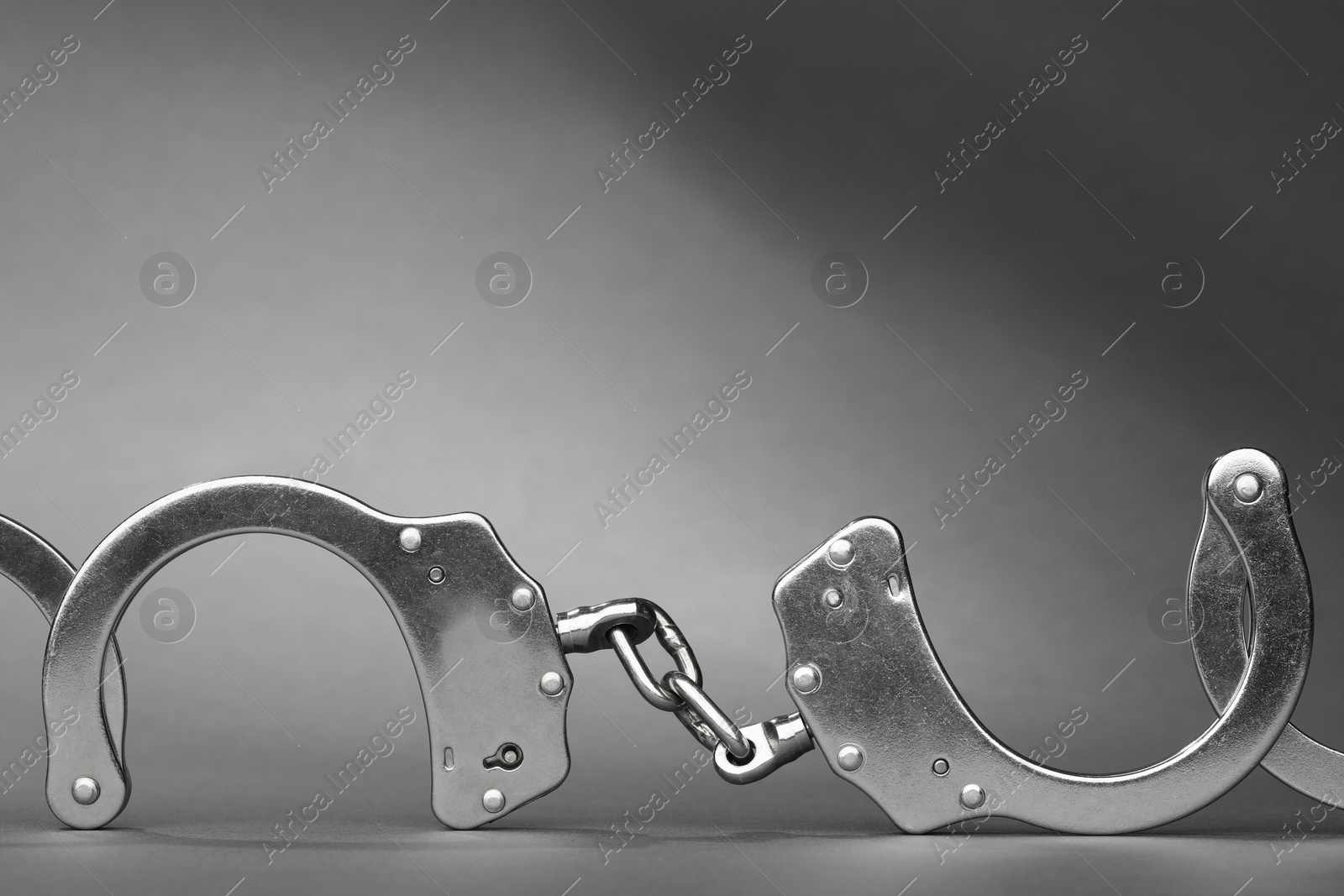 Photo of Metal chain handcuffs on grey background, closeup. Space for text