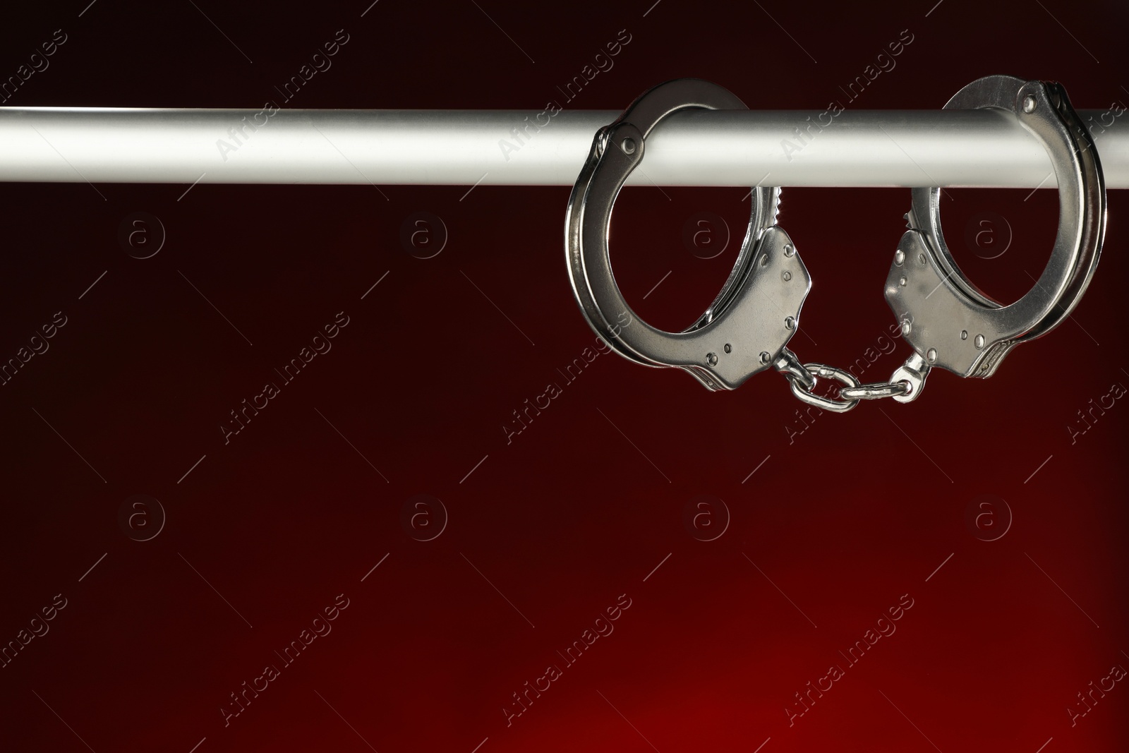 Photo of Metal chain handcuffs on pipe against dark background, closeup. Space for text