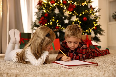 Photo of Little kids writing letter to Santa Claus on floor at home. Christmas celebration