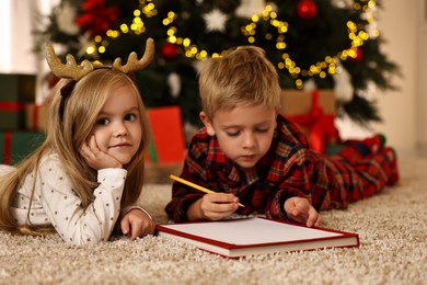 Photo of Little kids writing letter to Santa Claus on floor at home. Christmas celebration