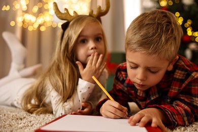 Photo of Little kids writing letter to Santa Claus on floor at home. Christmas celebration