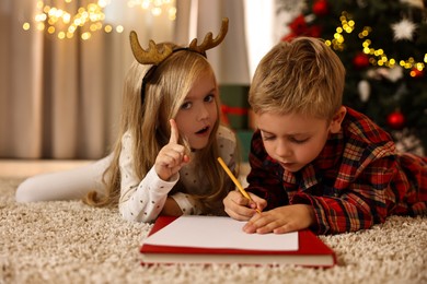 Photo of Little kids writing letter to Santa Claus on floor at home. Christmas celebration