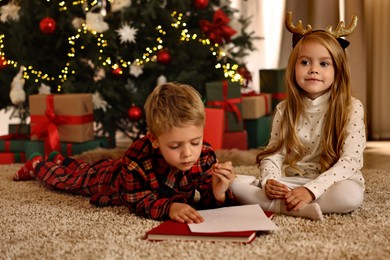 Little kids writing letter to Santa Claus on floor at home. Christmas celebration