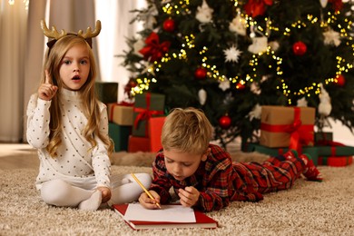 Photo of Little kids writing letter to Santa Claus on floor at home. Christmas celebration