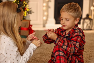 Photo of Little kids with candy canes on floor at home. Christmas celebration