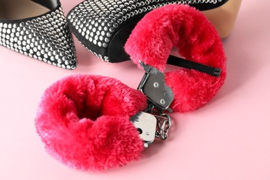 Photo of Fluffy handcuffs and high-heeled shoes on pink background, closeup