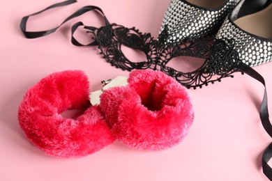 Photo of Fluffy handcuffs, lace mask and high-heeled shoes on pink background, closeup