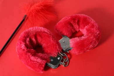 Photo of Pink fluffy handcuffs and feather on color background, above view