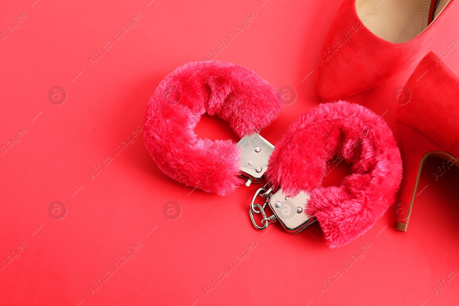 Photo of Pink fluffy handcuffs and high-heeled shoes on color background, flat lay. Space for text