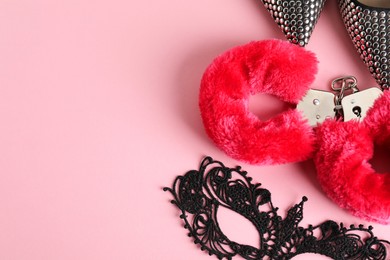 Photo of Fluffy handcuffs, lace mask and high-heeled shoes on pink background, flat lay. Space for text