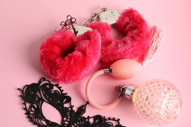 Photo of Fluffy handcuffs, lace mask and perfume bottle on pink background, above view