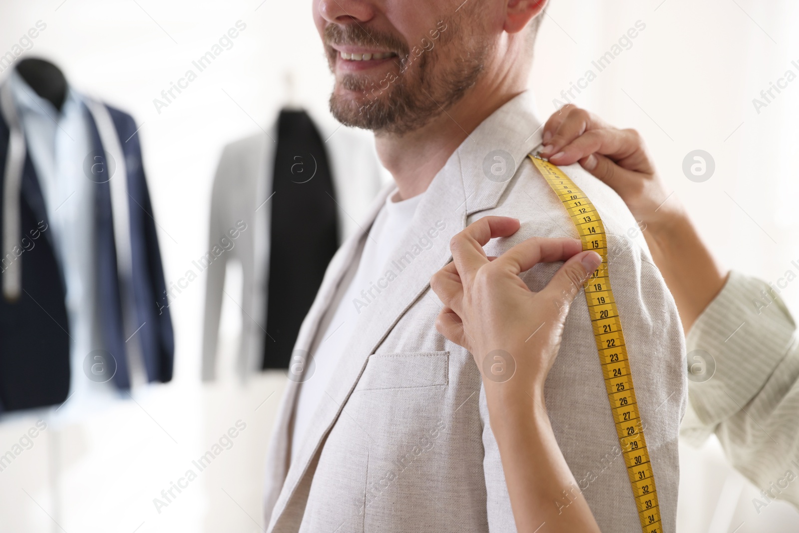 Photo of Woman measuring jacket shoulder on man in atelier, closeup