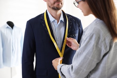 Photo of Tailor measuring jacket on man during fitting in atelier, closeup