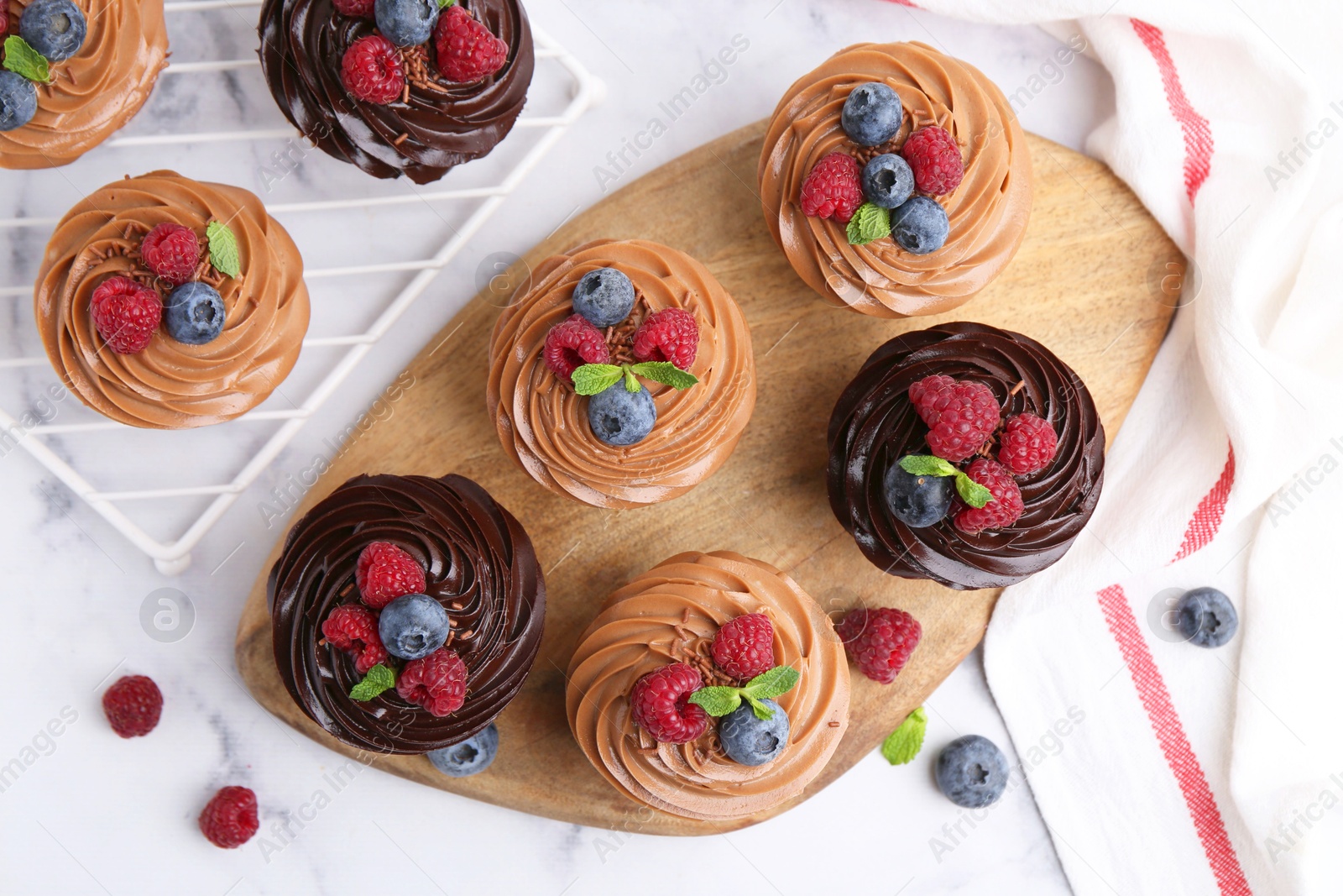 Photo of Tasty cupcakes with chocolate cream and berries on white marble table, flat lay