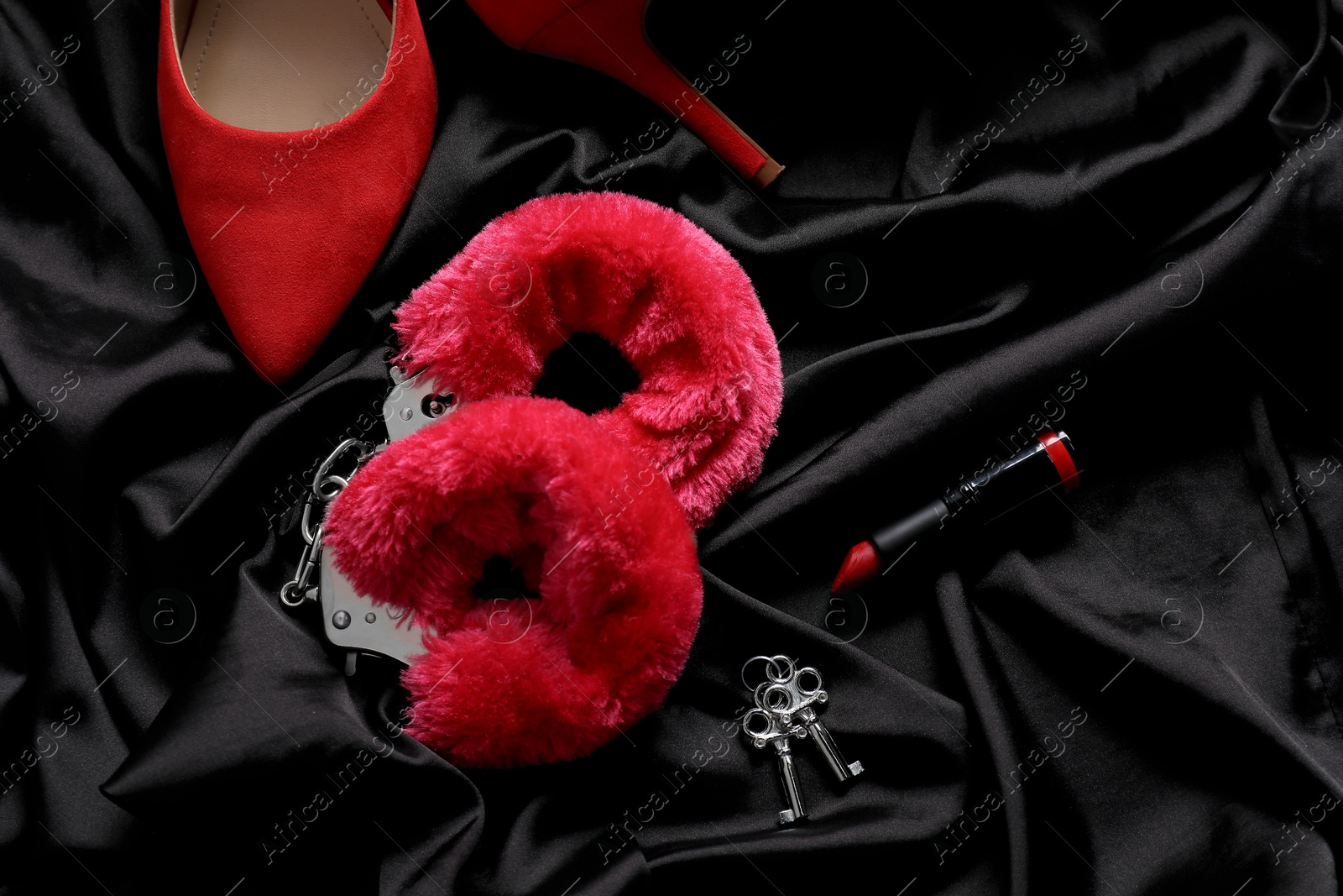 Photo of Red fluffy handcuffs, keys, shoes and lipstick on black fabric, flat lay