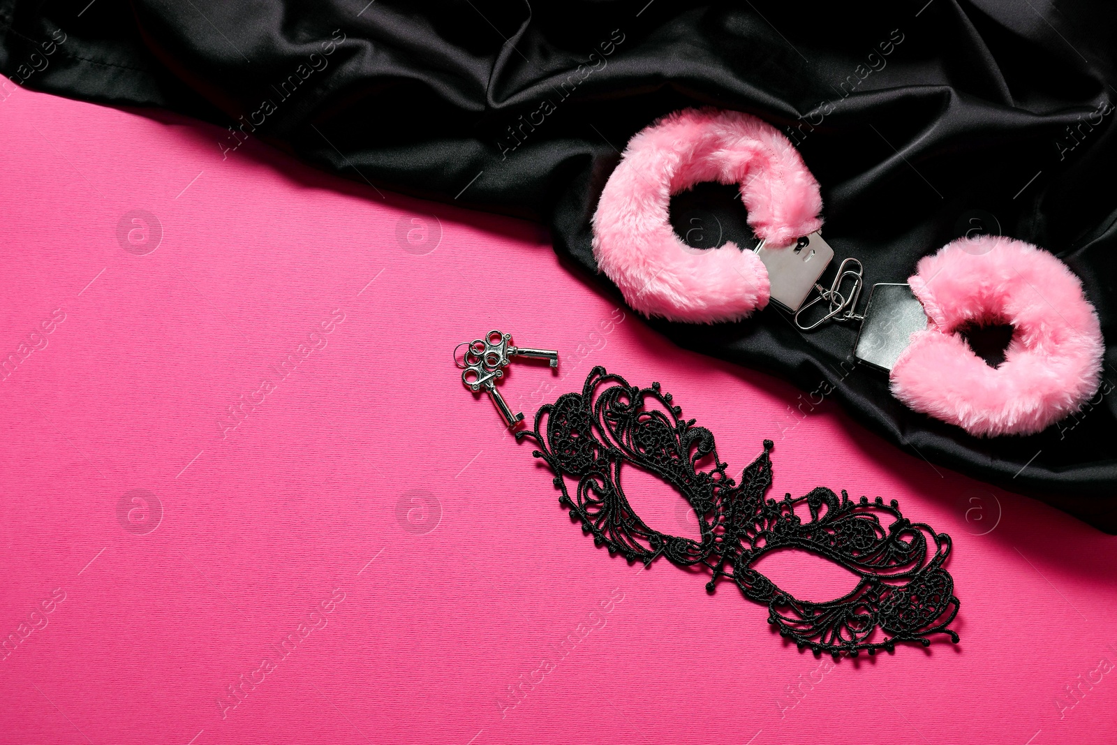 Photo of Fluffy handcuffs, keys, lace mask and black fabric on pink background, flat lay. Space for text