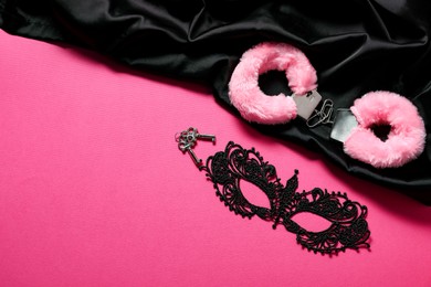 Photo of Fluffy handcuffs, keys, lace mask and black fabric on pink background, flat lay. Space for text