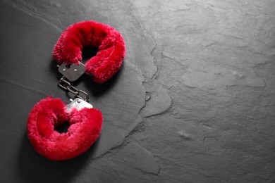 Photo of Red fluffy handcuffs on black textured surface. Space for text