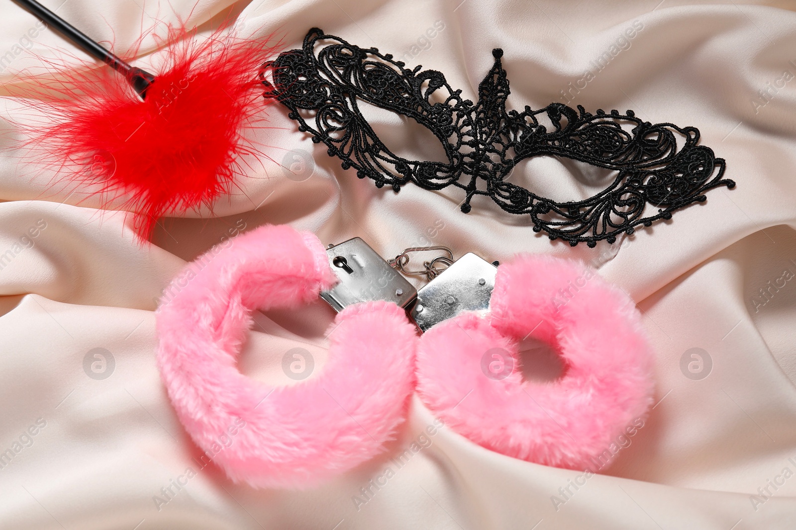 Photo of Pink fluffy handcuffs, feather and lace mask on beige fabric