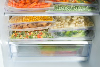 Photo of Plastic bags with different frozen vegetables in refrigerator, closeup