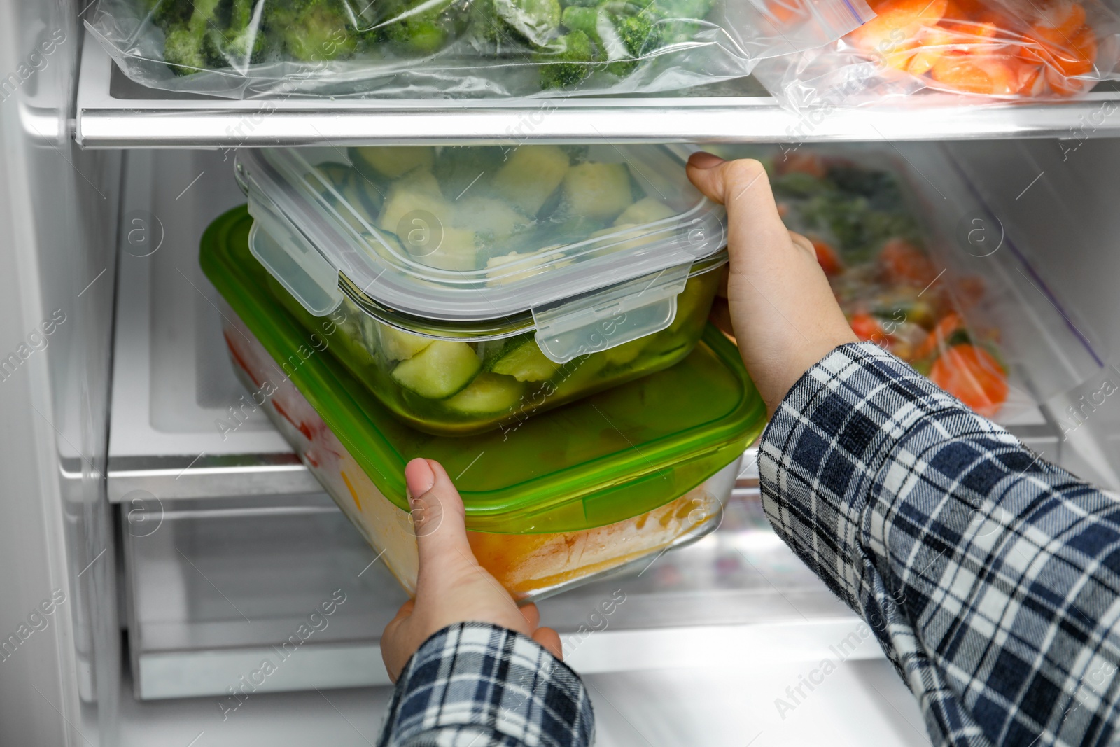 Photo of Woman taking glass containers with frozen vegetables from refrigerator, closeup