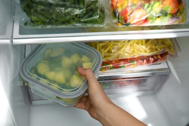 Photo of Woman taking glass container with frozen chopped zucchini from refrigerator, closeup