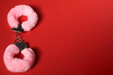 Photo of Pink fluffy handcuffs on red background, space for text