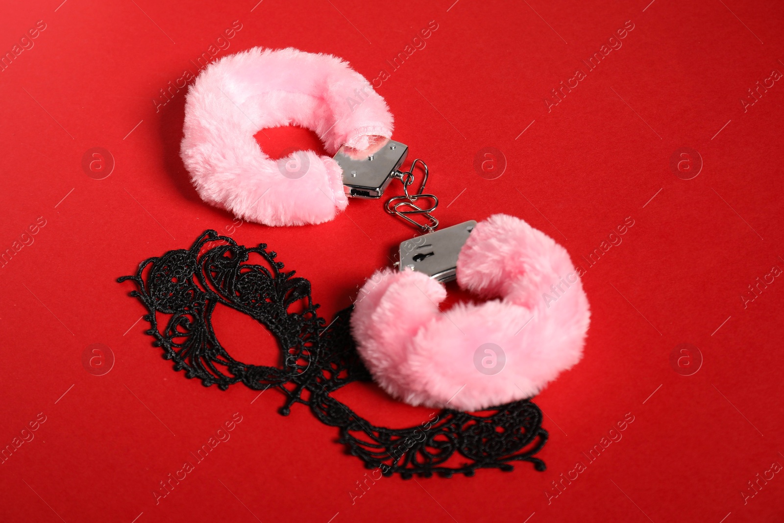 Photo of Pink fluffy handcuffs and lace mask on red background