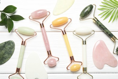 Photo of Face rollers, gua sha tools and green leaves on white wooden background, flat lay