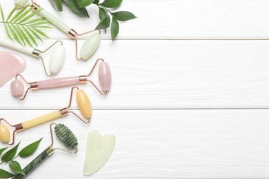 Photo of Face rollers, gua sha tools and green leaves on white wooden background, flat lay. Space for text