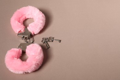 Photo of Pink fluffy handcuffs and keys on dark beige background. Space for text