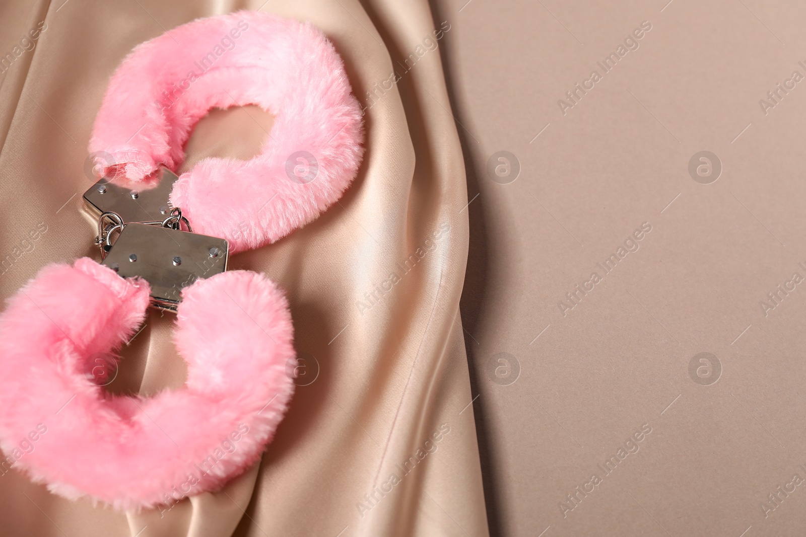 Photo of Pink fluffy handcuffs and fabric on dark beige background. Space for text