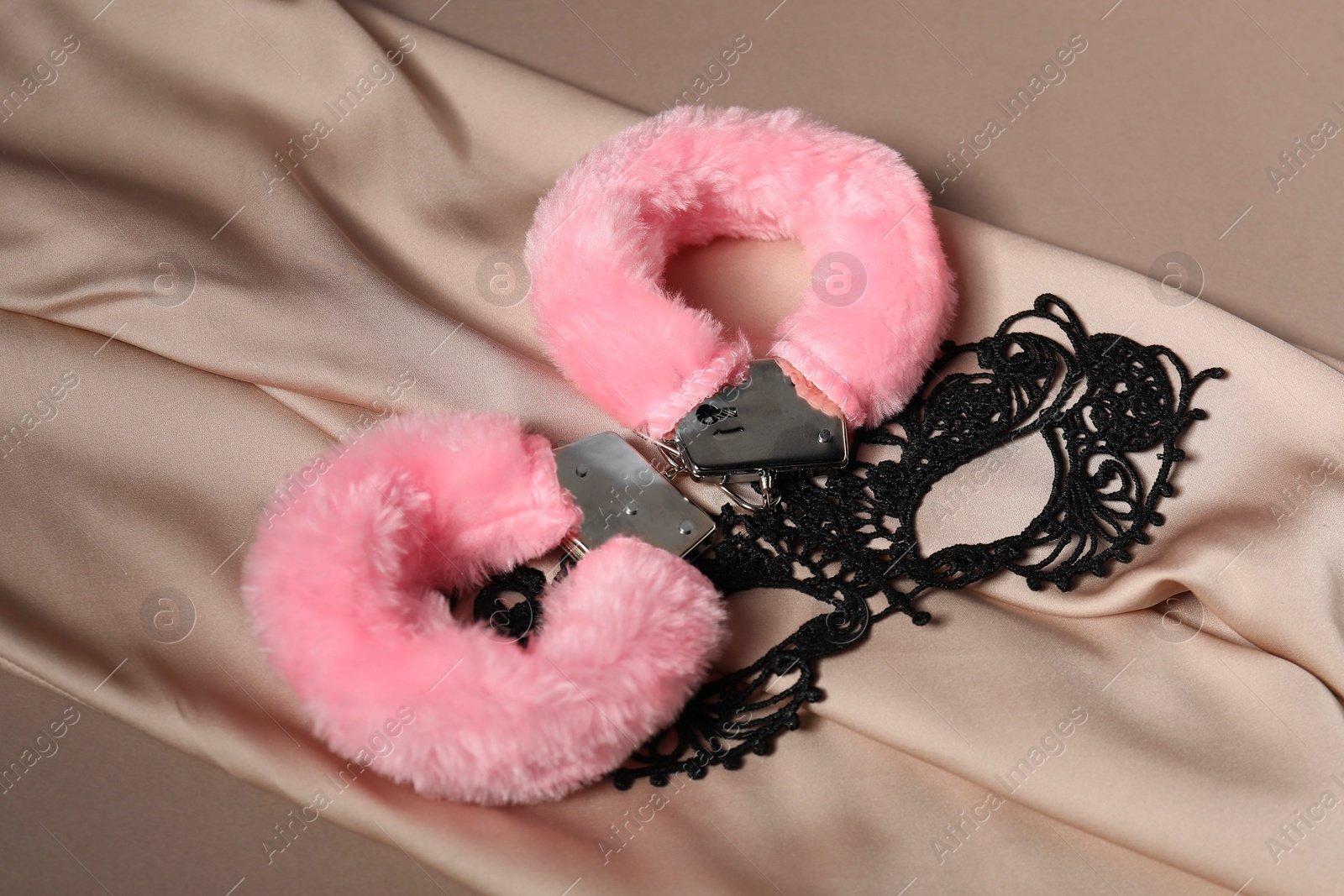 Photo of Pink fluffy handcuffs, lace mask and fabric on dark beige background. Space for text