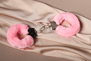 Photo of Pink fluffy handcuffs and fabric on dark beige background