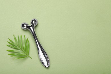 Photo of Metal face roller and palm leaf on green background, flat lay. Space for text