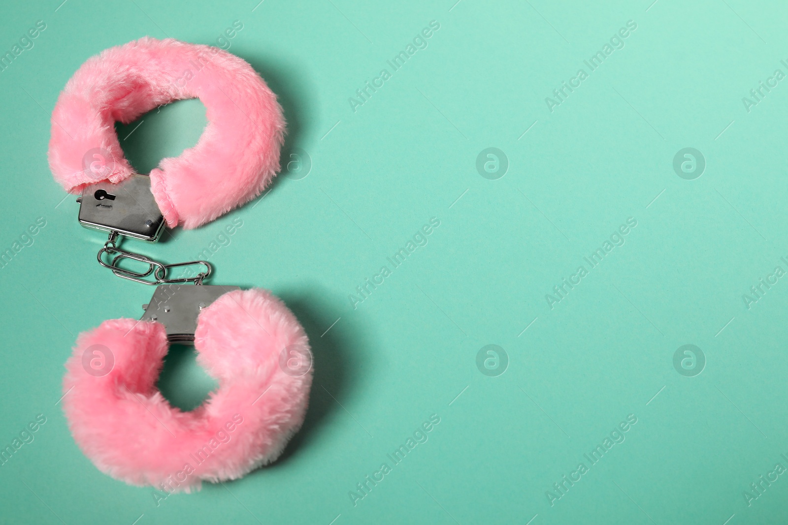 Photo of Bright fluffy handcuffs on turquoise background. Space for text