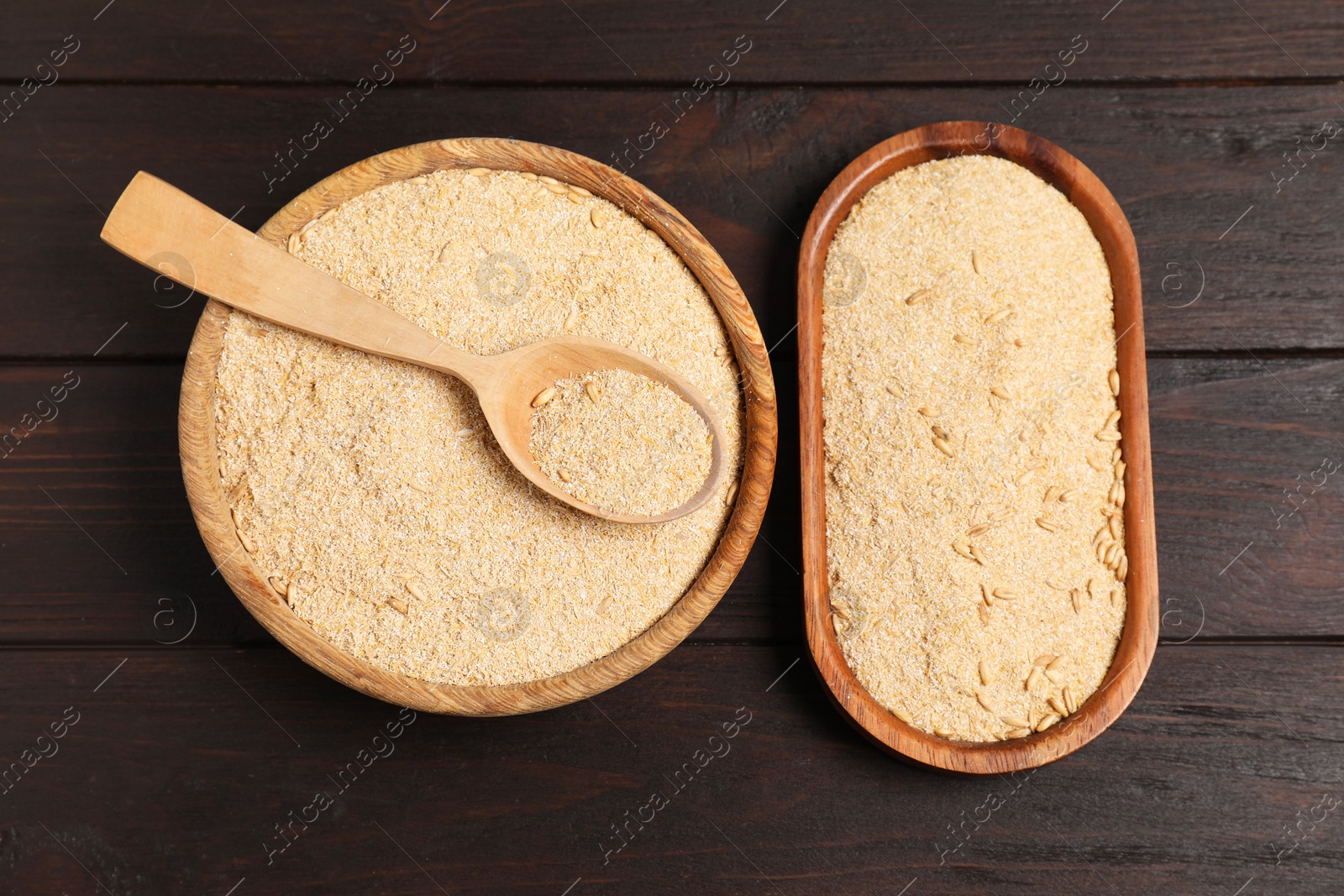 Photo of Oat bran in bowl, spoon and plate on wooden table, top view