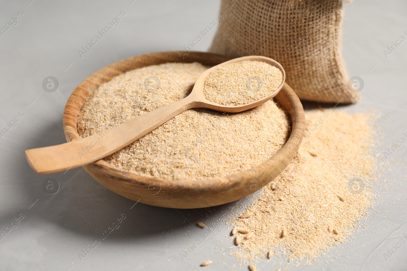 Photo of Oat bran in bowl and wooden spoon on grey table, closeup