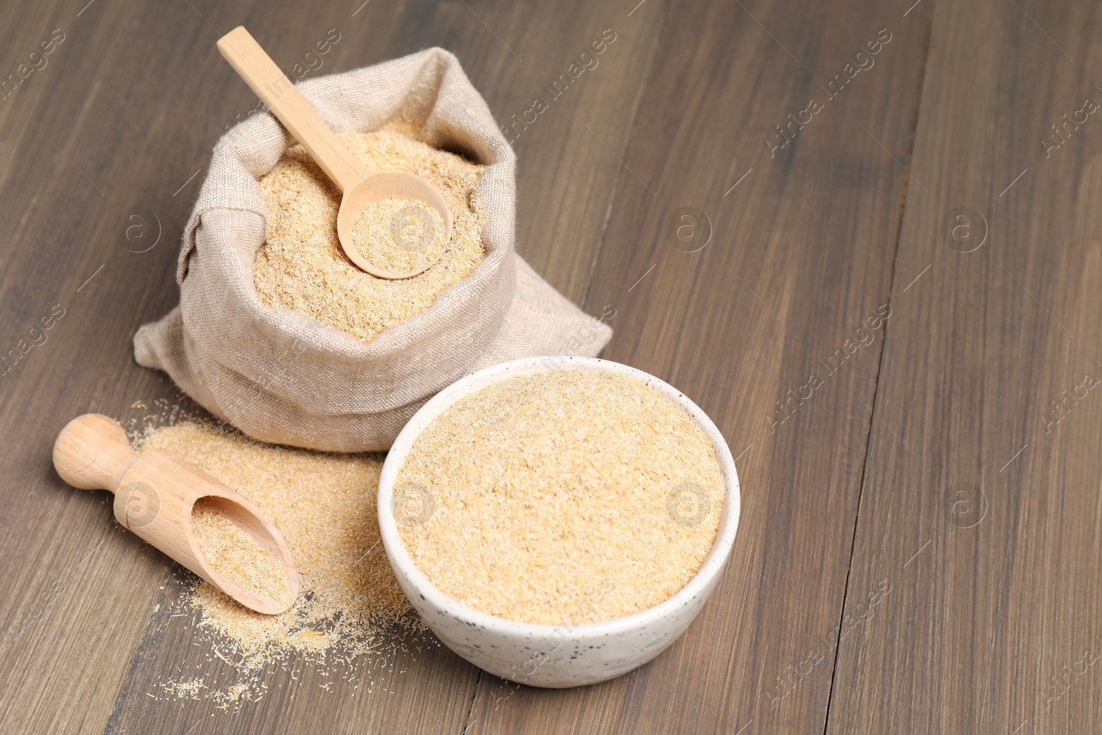 Photo of Oat bran in bowl, scoop, spoon and burlap bag on wooden table, space for text