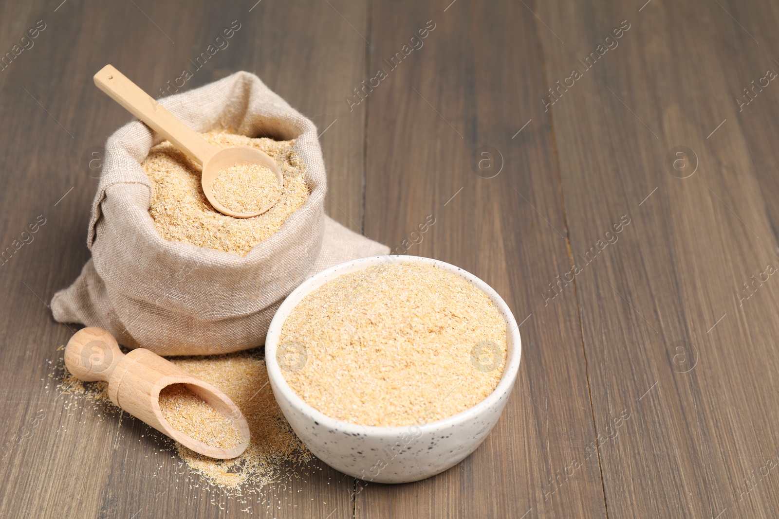 Photo of Oat bran in bowl, scoop, spoon and burlap bag on wooden table, space for text