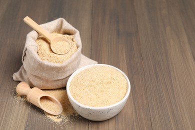 Photo of Oat bran in bowl, scoop, spoon and burlap bag on wooden table, space for text