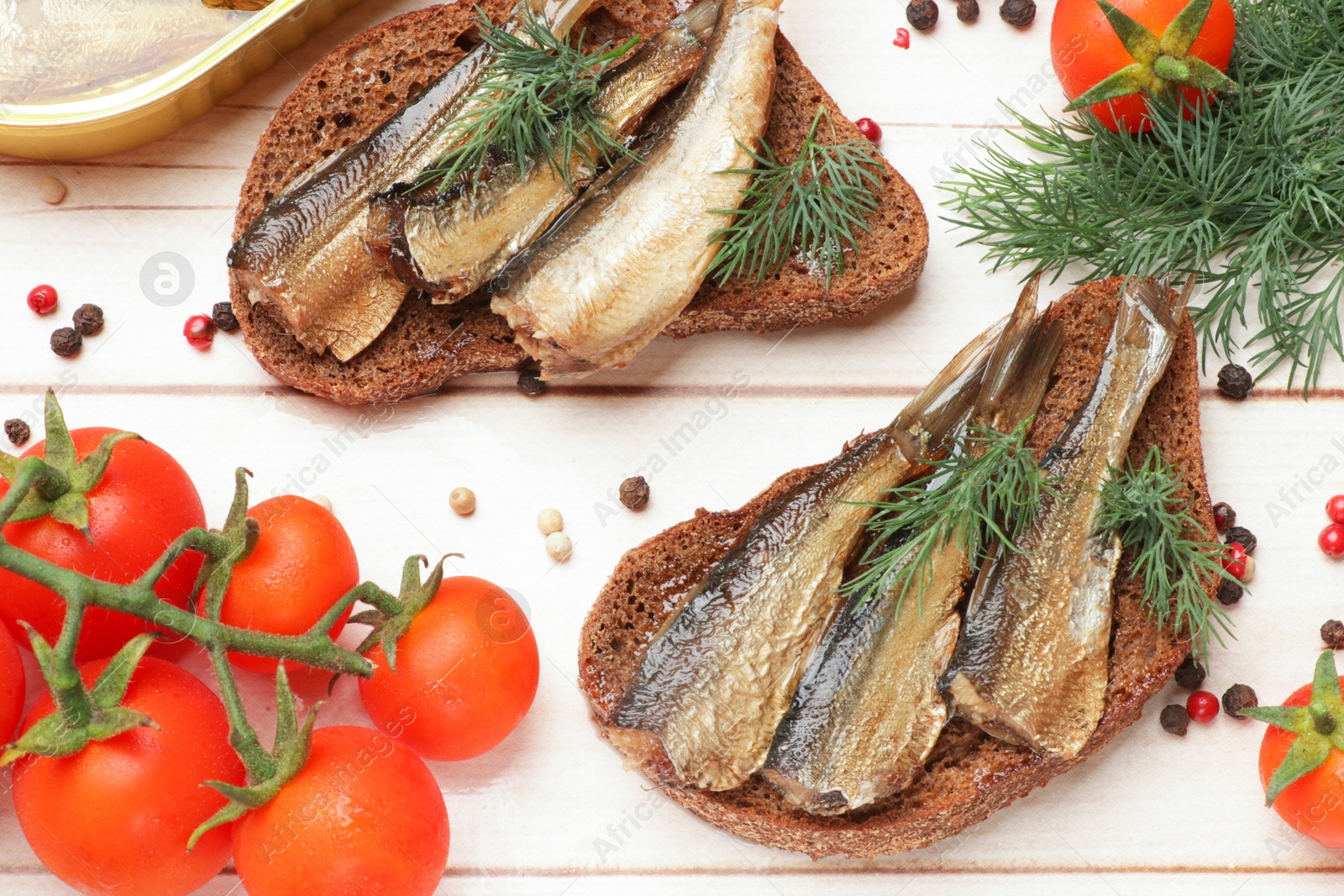 Photo of Delicious sandwiches with sprats and dill served on white wooden table, flat lay