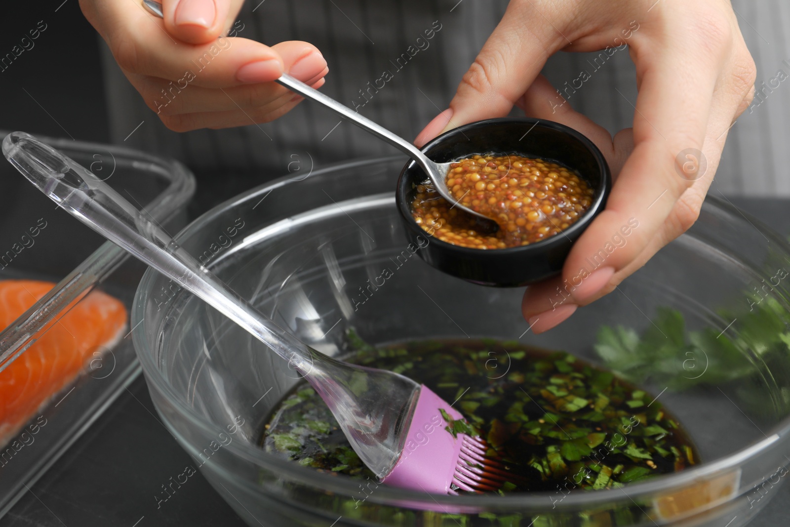 Photo of Woman adding mustard into bowl with soy marinade at dark gray table, closeup